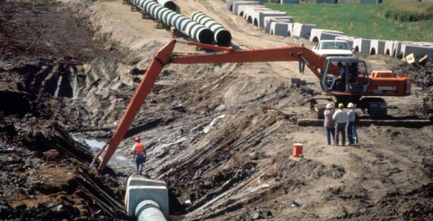 Excavator works on an exposed pipeline on a construction site