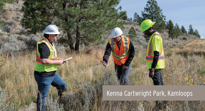 Three men wearing safety vests and hard hats stand in Kenna Cartwright Park