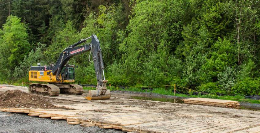 Excavator parked at a construction site beside a forest