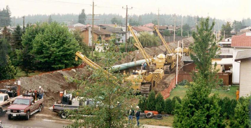 Multiple cranes and trucks lined along a pipeline trench