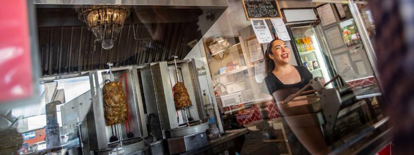 Smiling woman stands behind the counter of a donair shop