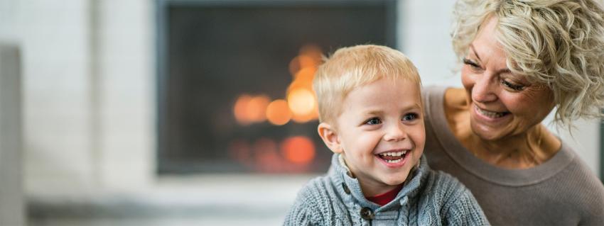 Woman smiles at young boy sitting with her with a fireplace in the background