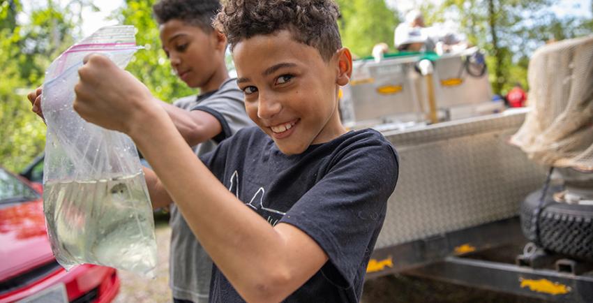 Boy holds plastic bag filled with water and two salmon smolts to release into a creek