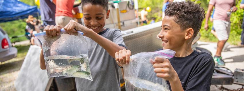 Two smiling boys hold plastic bags filled with water and salmon fry