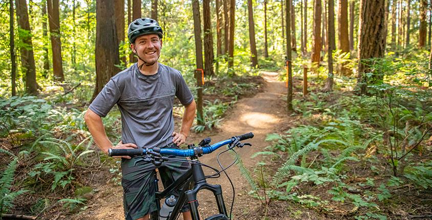 Man sitting on a mountain bike on a bike trail in the Riverview Forest smiles at the camera
