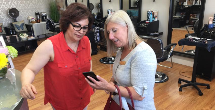 Two women in a hair salon look at a cell phone