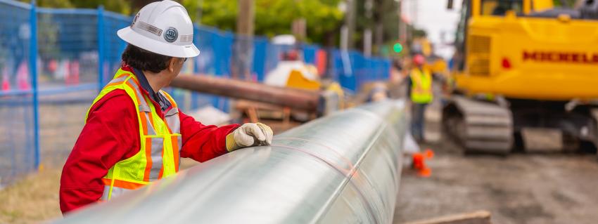 Man in safety gear with a hand on a pipeline