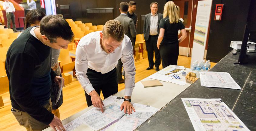 Two men look at blueprint drawings during a public meeting