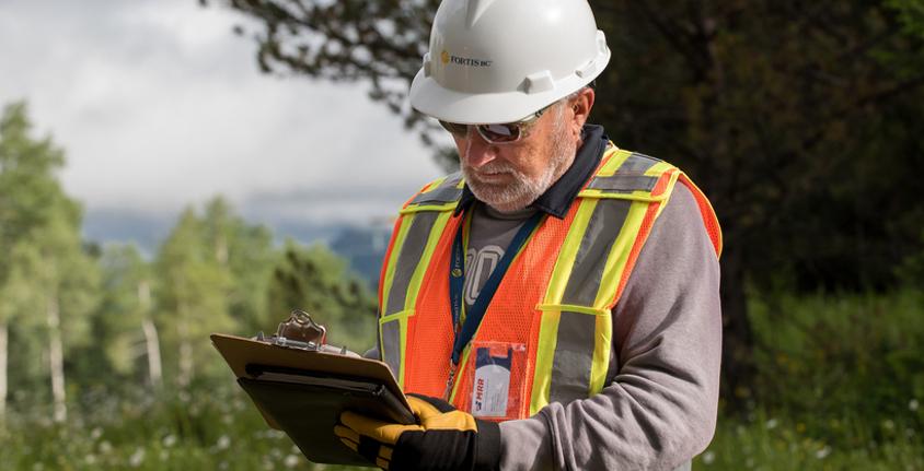 Man in FortisBC hard hat holds a clip board