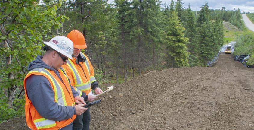 Two people wearing orange safety vests review an ipad while standing along a work site on the Inland Gas Upgrades project route