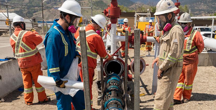 Workers wearing protective gear run pigging equipment through a pipe