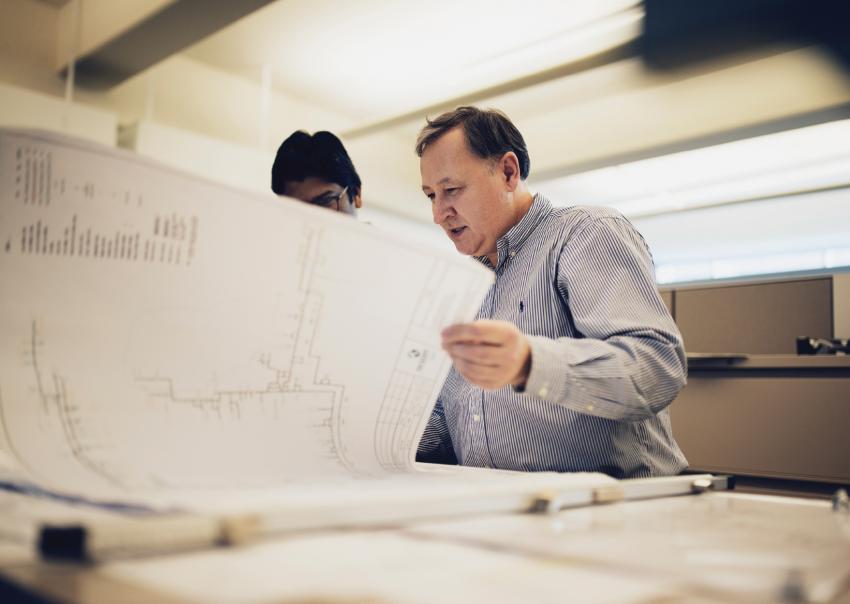 Two people review blueprint drawings in an office