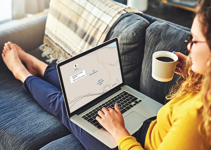 Woman lies on a couch with a coffee in her hand and a laptop on her lap