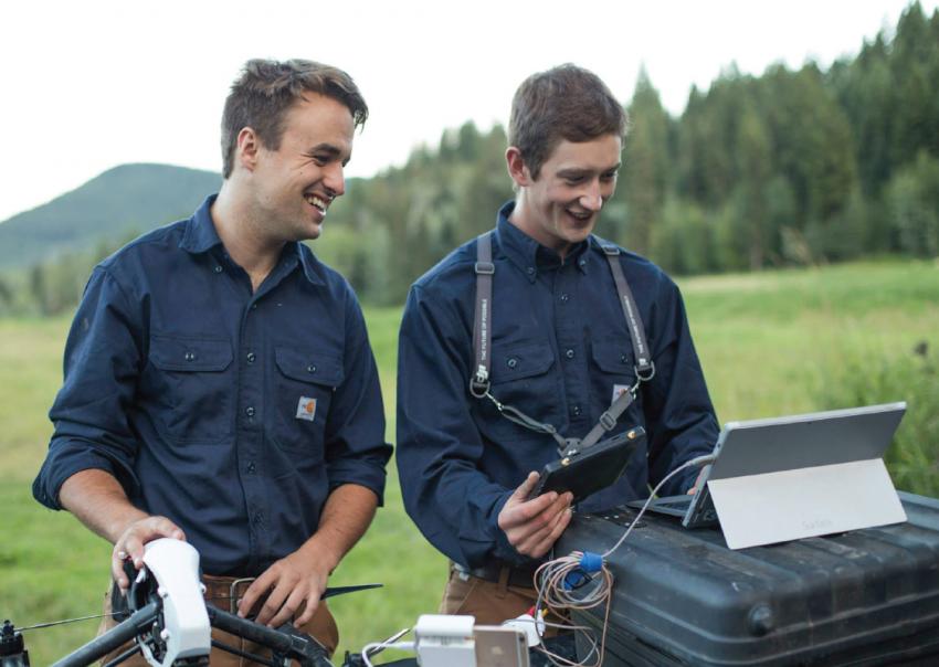 Man holds a drone while another man reviews computer data