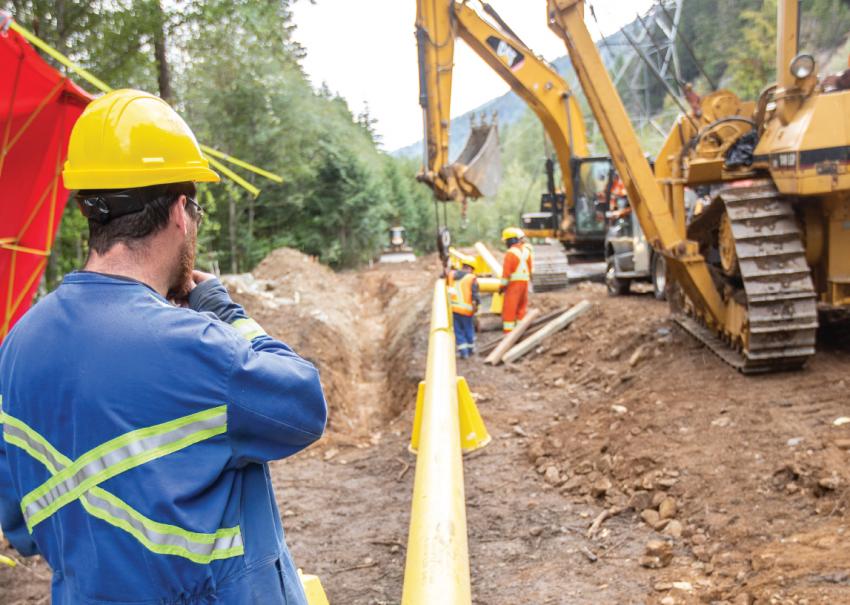 Worker with back to the camera watches an excavator working on a pipeline