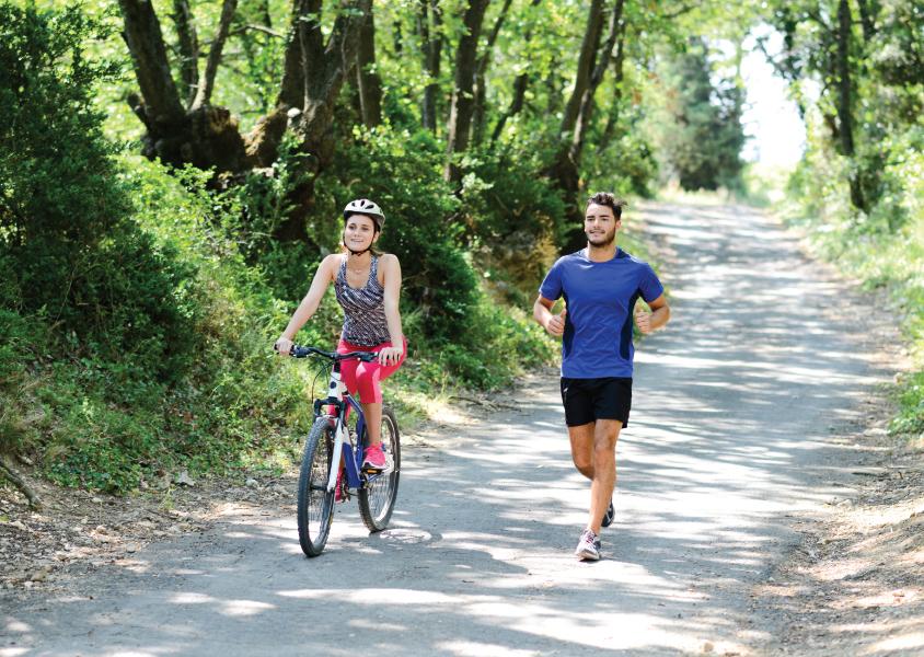 Woman rides a bike alongside a man running on the multi-use pathway in Burnaby