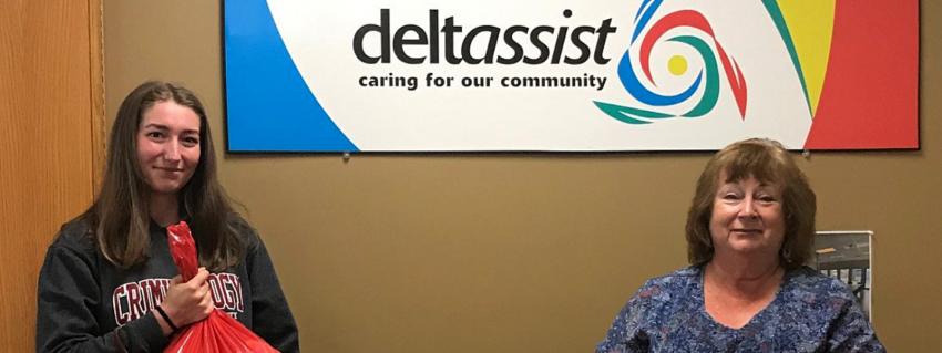 Two women stand in front of a deltassist sign