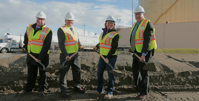 Four people wearing hard hats and safety vests each hold a shovel of dirt at the Tilbury expansion ground breaking ceremony