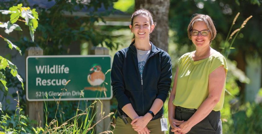 Two women smile at the camera, standing beside a Wildlife Rescue sign