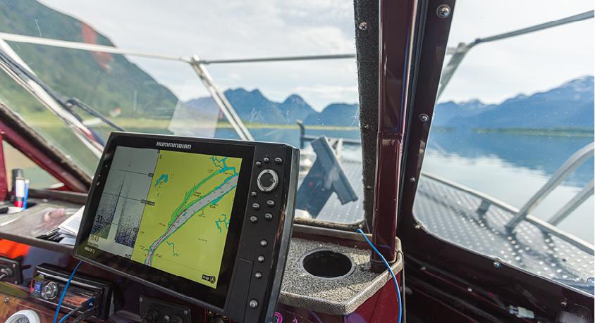 A computer screen shows navigation at the helm of a boat on the water
