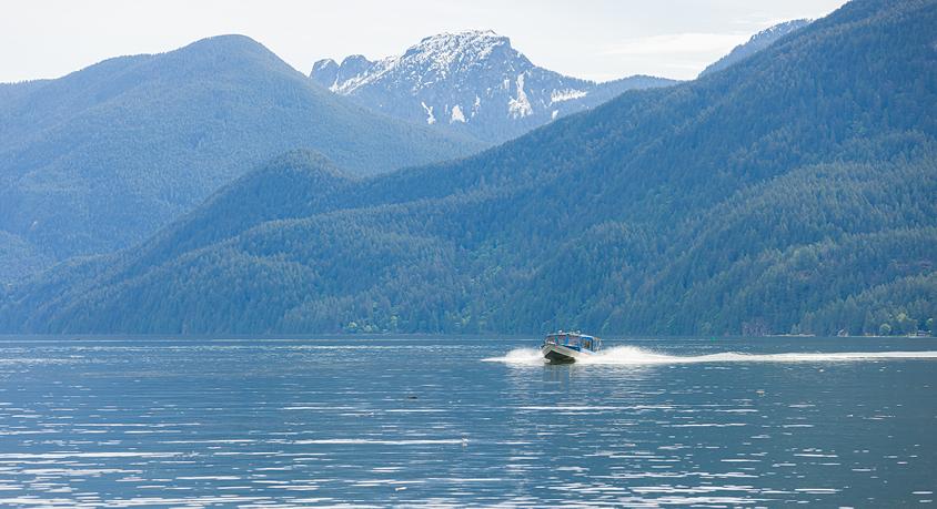 a boat drives through calm water leaving a wake with mountains in the background