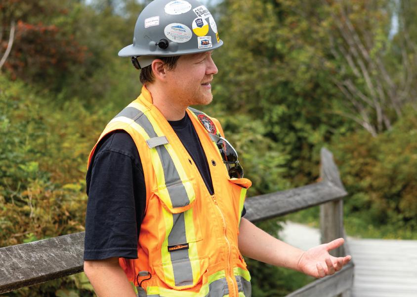 Michael Mroczkowski stands talking to someone off-carmera. He is wearing a safety vest and hard hat.