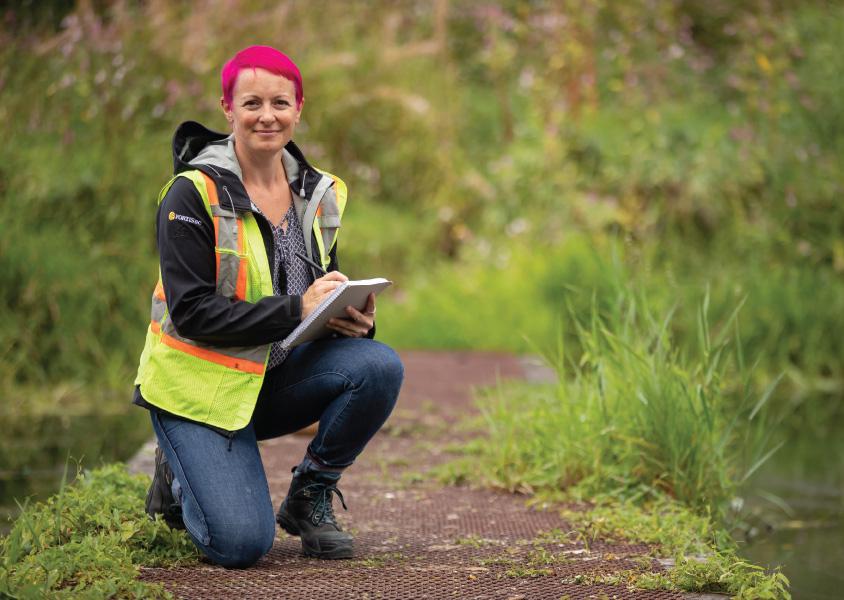 Caroline Astley kneels along a path at Burnaby Lake park