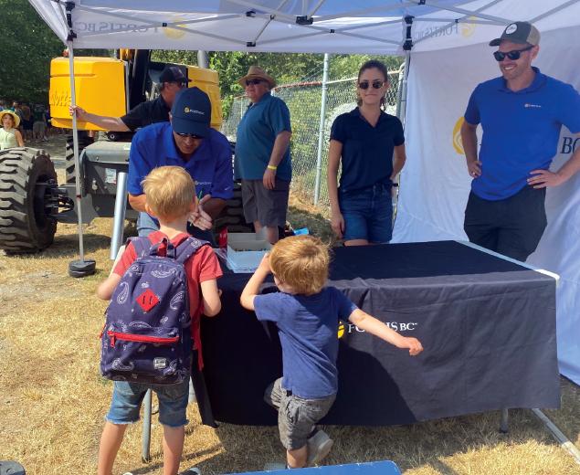 Children interacting with people at a FortisBC booth under a tent, with equipment in the background