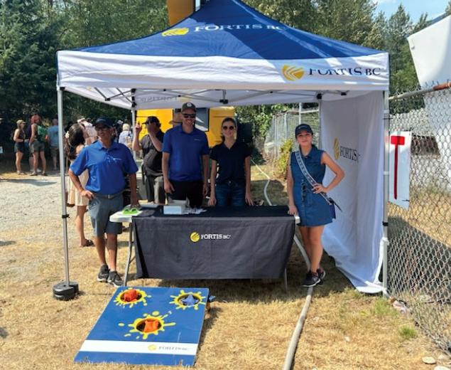 People at a FortisBC booth with a bean bag toss game board outside