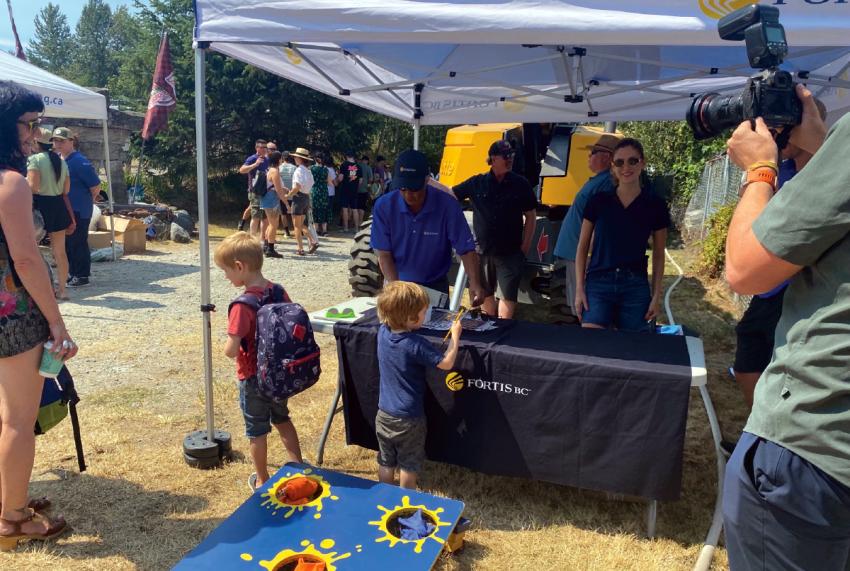 Children interacting at a FortisBC booth during outdoor event, with adults and photographer nearby