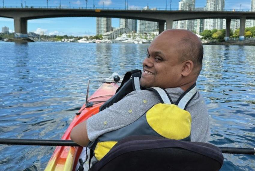 A person smiling while kayaking on a river with a cityscape and bridge in the background