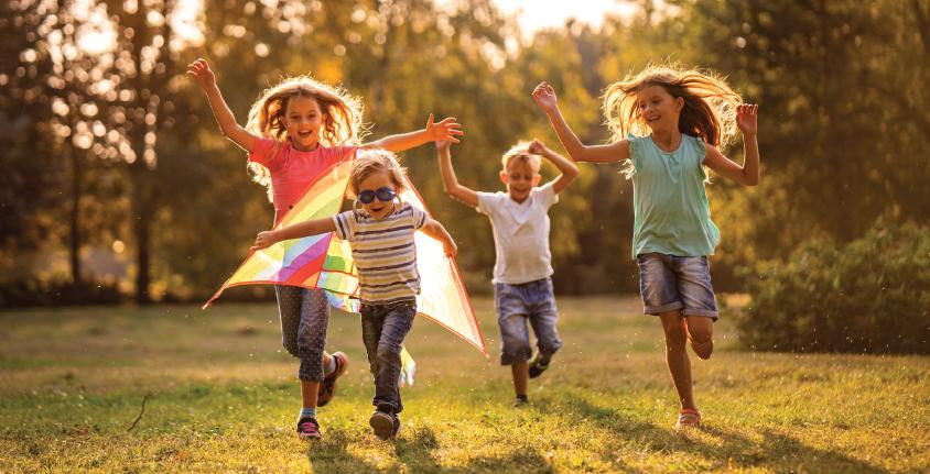 Children running joyfully with kite in golden sunlit field