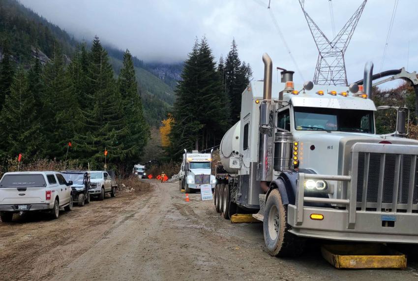 Two large trucks and three cars on a dirt road