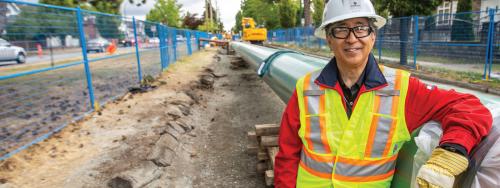 Man smiles at camera leaning on a pipeline under construction