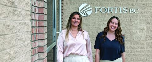 Two women smile outside a building with the FortisBC logo in the background