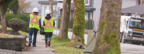Two FortisBC workers walk down a sidewalk away from the camera